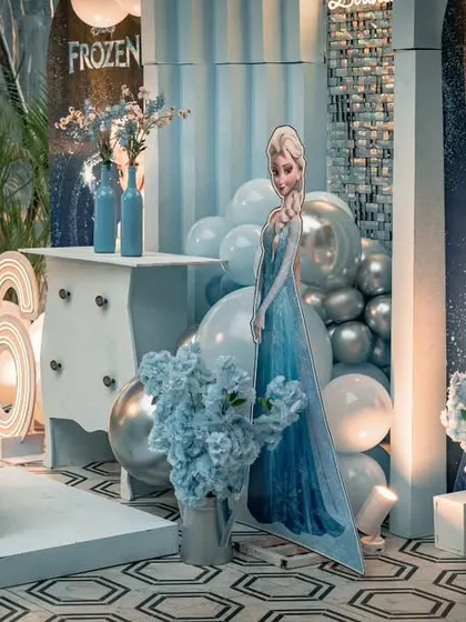 A full view of the Frozen birthday setup, showcasing the custom backdrop with Susrutha's name and age. The silver and blue balloons create a chilly, magical atmosphere perfect for the theme.