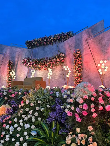 A modern and artistic reception stage with angled concrete-style panels, adorned with beautiful pink and purple floral arrangements.