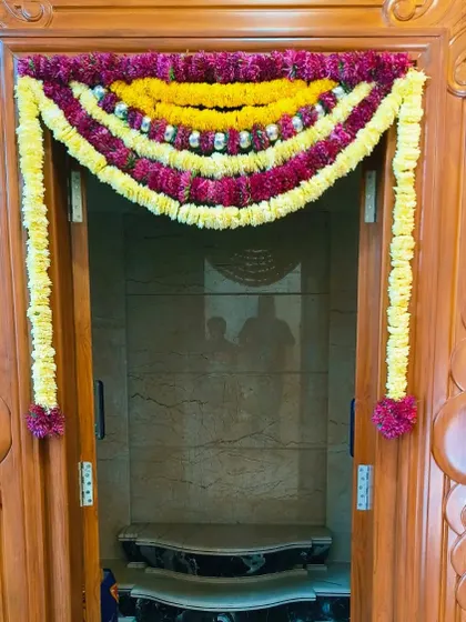 A simple flower toran for a pooja room door, made with yellow and magenta flowers and accented with silver balls.