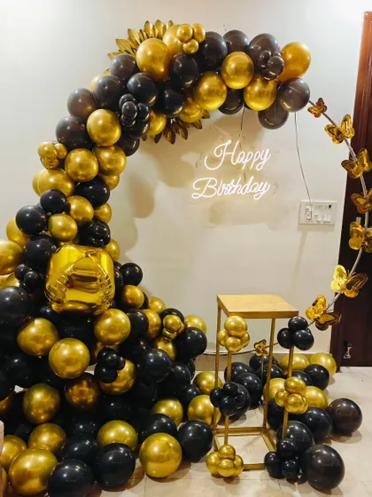 A luxurious black and gold birthday setup. This half-circle balloon arch is accented with gold butterflies and a neon sign for a touch of elegance.