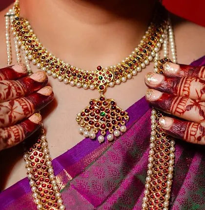 The bride's hands framing her traditional temple jewelry, with the deep red of the henna stain adding to the richness of the look.