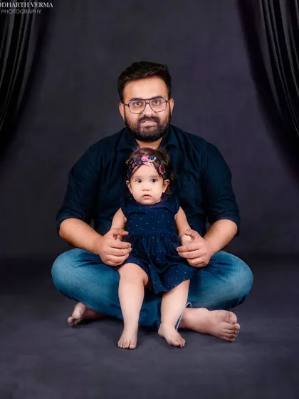 A father and his baby daughter sit together for a portrait. The simple, dark background puts all the focus on their sweet connection.