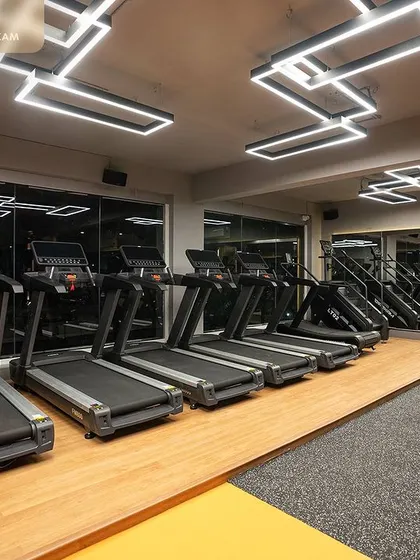 The cardio section features a line of treadmills against a wall of mirrors, maximizing light and space. We installed geometric overhead lighting to add a contemporary design element to this functional workout zone.