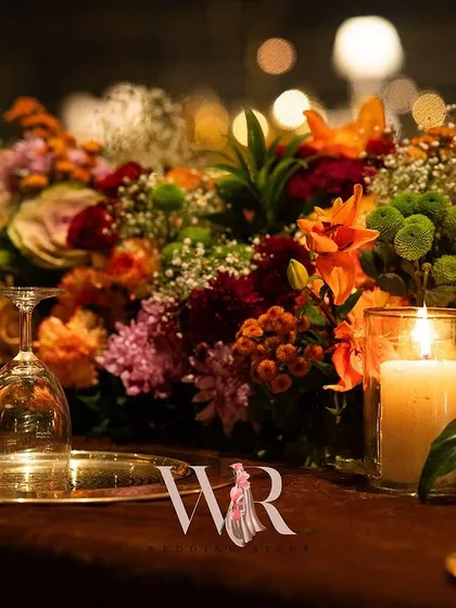A close-up of a long table runner made of burnt orange, red, and green florals. The textures and colors create a rich, autumnal feel, perfect for a winter wedding.