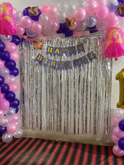 A princess-themed first birthday party with a balloon arch over a silver foil curtain and princess foil balloons.