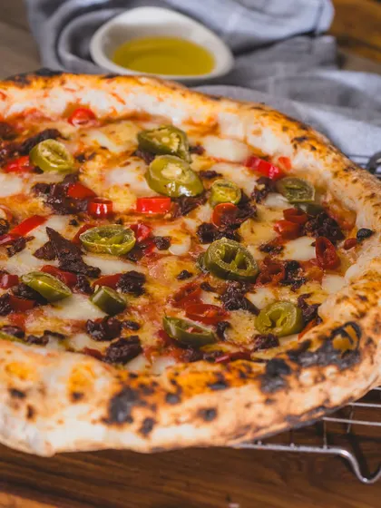 A spicy pizza topped with jalapeños and cured meat, resting on a cooling rack. The flavours are as bold as the colours.