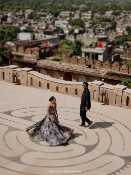 A tilt-shift style photograph shows the couple on a labyrinth pattern at Six Senses Fort Barwara, with the historic town in the background.