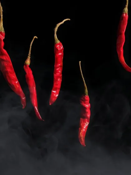 A creative shot of red chillies appearing to float in the air, with a hint of smoke below them. This levitation effect gives a simple ingredient a magical and mysterious quality.
