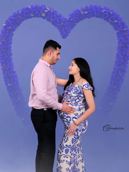 A beautiful studio portrait of a couple, with the mother-to-be in a blue and white sequined gown, framed by a heart-shaped floral graphic.