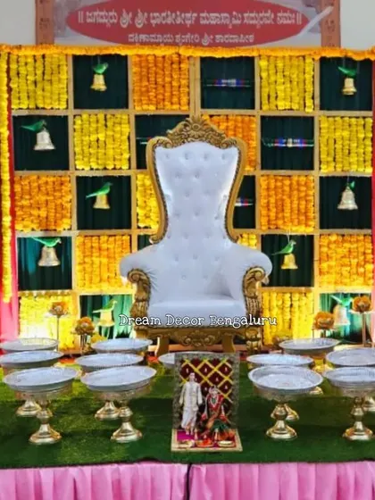 A traditional baby shower backdrop with a checkerboard of marigolds and bells. The setup includes a throne for the mom-to-be and a display of plates, creating a classic and festive look.