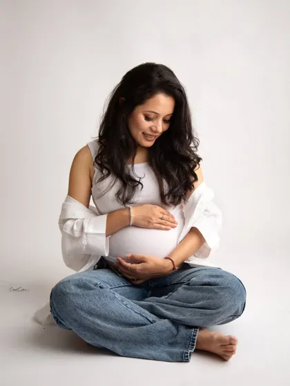 A beautiful, candid-style moment. The mom-to-be looks down at her bump with a sweet smile, her casual outfit perfect for this intimate portrait.