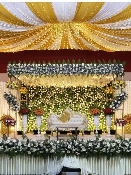 We create stunning, large-scale reception stages like this one, featuring a beautiful floral wall, elegant drapery, and coordinated ceiling decor with fairy lights to create a magical ambiance for your special day.