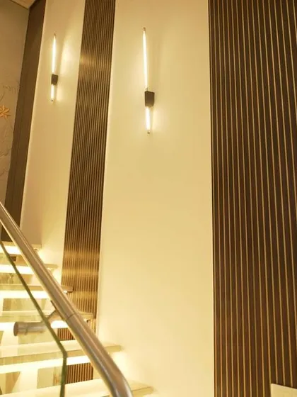 The upper part of the staircase, with glass railings and modern wall sconces set against fluted wooden panels.