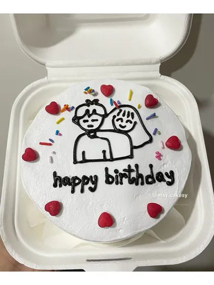 A cute couple drawing on a birthday bento cake, decorated with sprinkles and hearts.