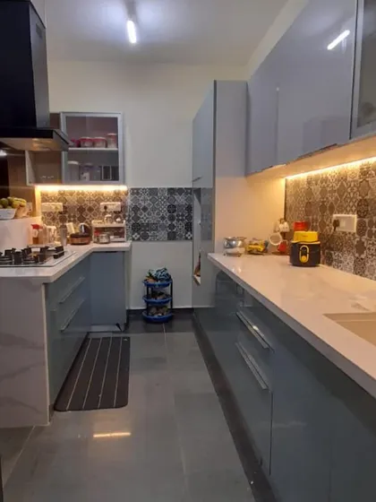 A sleek parallel kitchen with glossy grey cabinets and handle-less drawers. The design is complemented by patterned backsplash tiles and under-cabinet LED lighting, creating a bright and modern cooking environment.