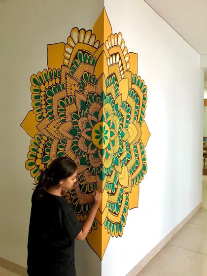 In the making of a corner mandala. The yellow and green design is painted across two walls, creating a unique 3D effect.
