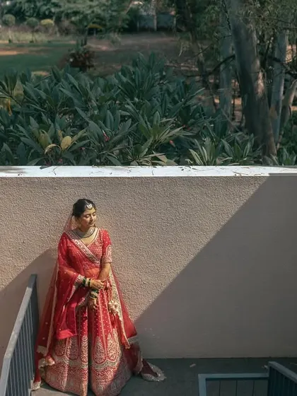 A beautifully lit bridal portrait. The bride stands on a staircase, the play of light and shadow creating a dramatic and elegant effect on her red lehenga.
