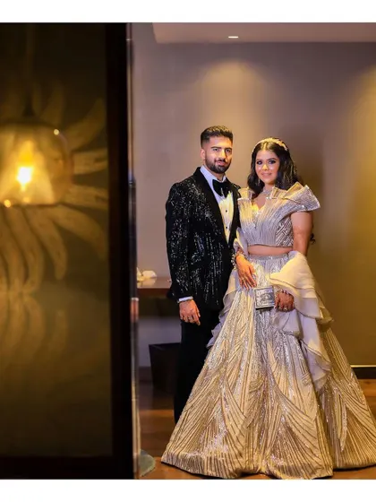 A formal portrait of the couple at their reception. The bride's unique, structured lehenga and the groom's classic tuxedo are captured in an elegant indoor setting.