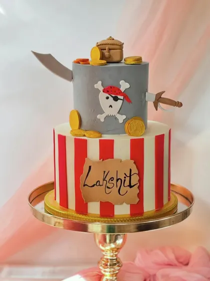 A two-tiered pirate adventure cake. The design includes a treasure map, gold coins, swords, and a skull and crossbones flag for a swashbuckling birthday.
