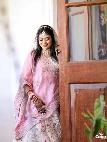 A lovely portrait of the bride in her pastel pink lehenga, peeking through a doorway.