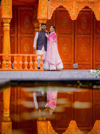 A stunning reflection shot of a couple in traditional pink outfits. The vibrant orange background and the clear reflection create a very artistic and colorful image.