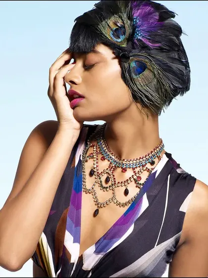 A beauty shot that incorporates natural elements like peacock feathers into a high-fashion context. The styling and pose create an image that is both elegant and slightly avant-garde.
