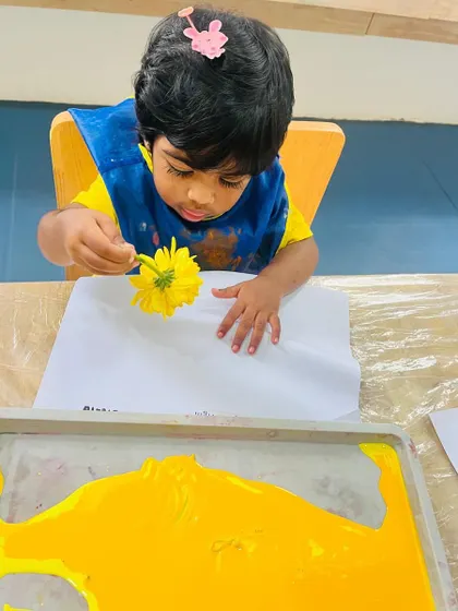 A toddler dips a flower into yellow paint, connecting with nature while creating beautiful imprints on paper.