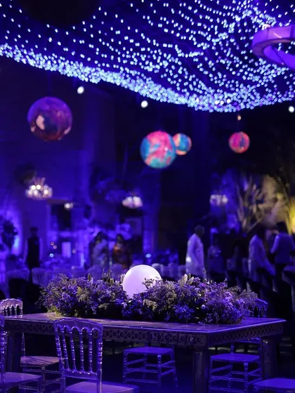 A closer look at the celestial-themed Sangeet decor. The centerpiece features a glowing orb surrounded by florals, with planet installations and a starry ceiling creating an immersive, otherworldly dining experience.
