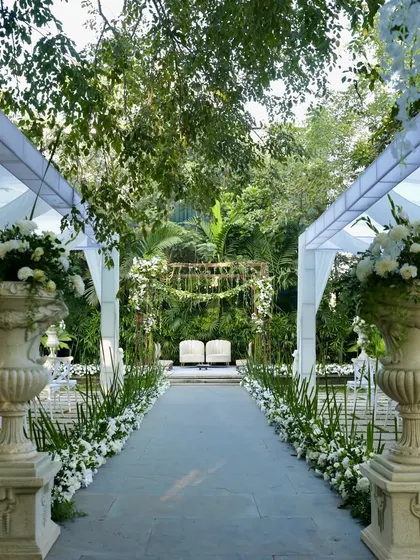 The beautiful aisle view of the white and green wedding, with large floral urns framing the path to the mandap.
