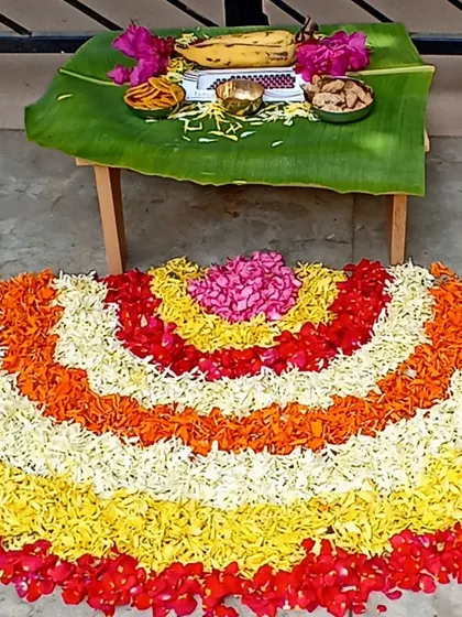 A semi-circular pookalam with a traditional 'vilakku' (lamp) and offerings on a banana leaf.