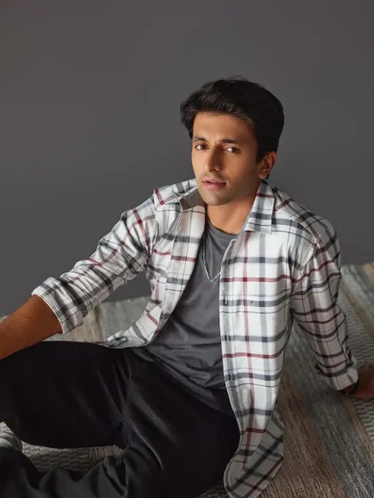 A catalogue shot for a men's casual wear brand. The makeup is minimal and clean, focusing on shine control and evening out the skin tone for a polished final image.