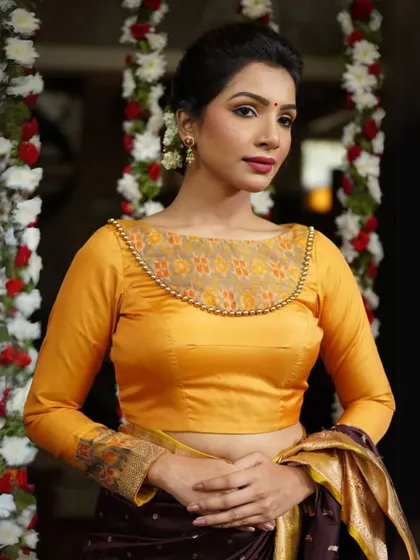 This long-sleeved yellow blouse has a sheer panel on the neckline, embellished with delicate beadwork. The cuffs are also adorned with a matching printed fabric.