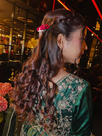 A detailed view of the party hairstyle. This braided half-up, half-down style with loose curls is a versatile and popular choice for festive occasions, adorned here with a small flower.