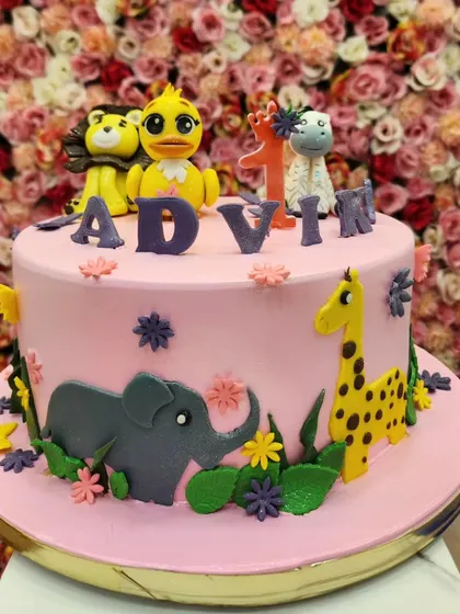A closer look at the pink jungle theme cake, personalized for Advik's first birthday. The fondant animals are friendly and colorful.