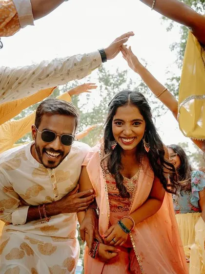 A candid shot of the couple laughing as they walk through an arch made by their friends during the Haldi ceremony.