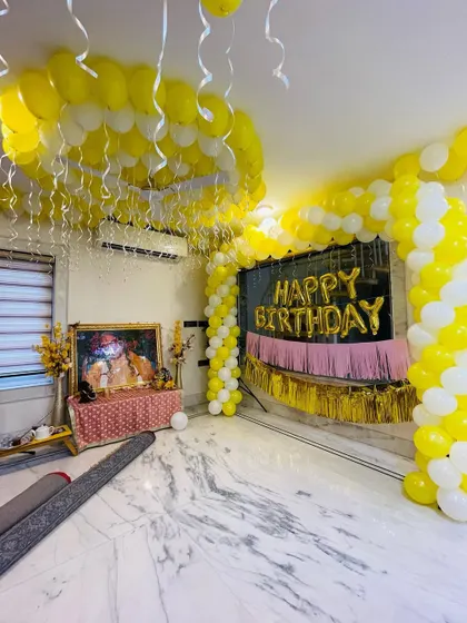 A bright and cheerful home decoration for a religious celebration. The room is filled with yellow and white balloons, including a ceiling canopy and a backdrop arch.