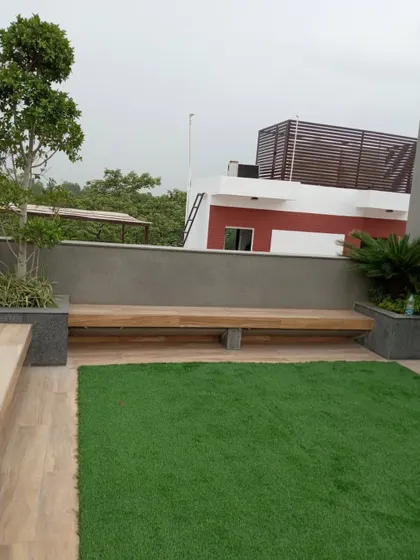 A minimalist rooftop garden in GK1 featuring a clean patch of artificial lawn next to a wooden deck. A long, low-profile wooden bench is integrated into the design, providing simple and functional seating.