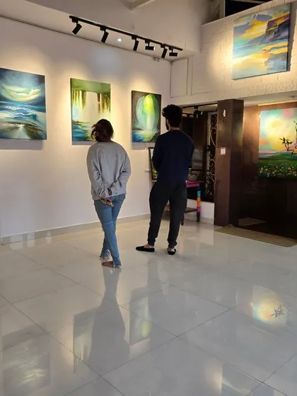 Two guests study the abstract waterfall paintings at Gurpreet Kaur's solo exhibition, reflecting on the artist's use of color and light.