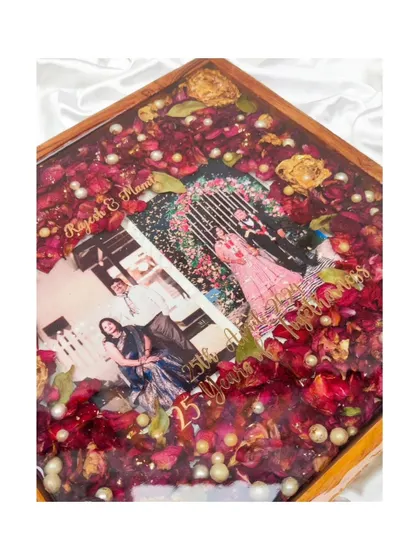 A close-up of the 25th-anniversary frame, showing two photos from the couple's journey together, surrounded by a bed of their preserved varmala flowers.