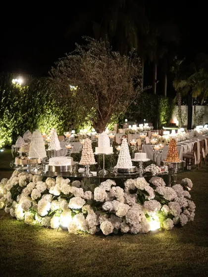 A spectacular circular dessert table surrounded by a bed of illuminated white hydrangeas. This grand display serves as a stunning centerpiece for the entire event space.