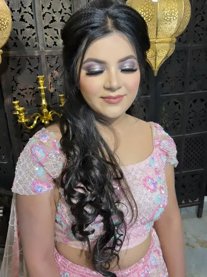 A princess-inspired engagement look. The soft pink lehenga is paired with a shimmery silver and pink eye makeup look and a side-swept curly hairstyle for a romantic feel.