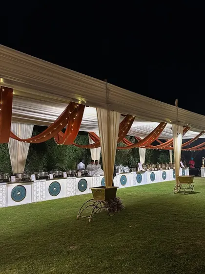 An elegant outdoor buffet setup under a tent, with rustic orange and cream drapes complemented by fairy lights.
