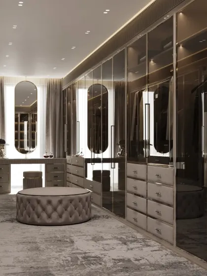 This closet design exudes a moody and sophisticated vibe with smoked glass doors and a dark color scheme. A plush, tufted ottoman sits at the center, providing a comfortable spot for dressing.