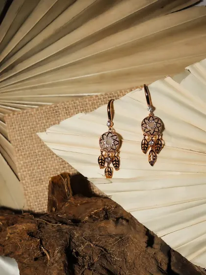 A pair of dreamcatcher-style earrings photographed with natural elements like wood and dried leaves. This setup creates a beautiful, organic aesthetic for a lifestyle brand's e-commerce page.