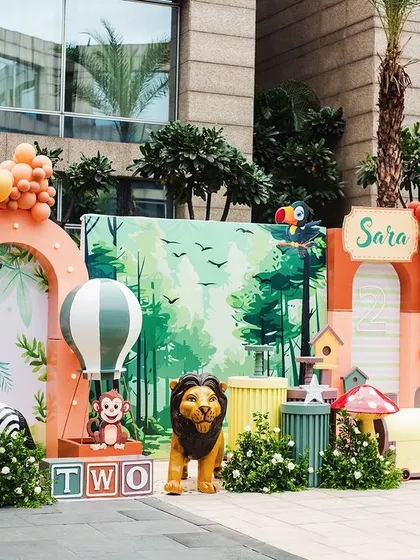 Sara's 'Wild Two' party was a vibrant jungle adventure. This full view shows the custom backdrop, life-sized animal props like a zebra and giraffe, a fun animal train, and colorful balloon arrangements.