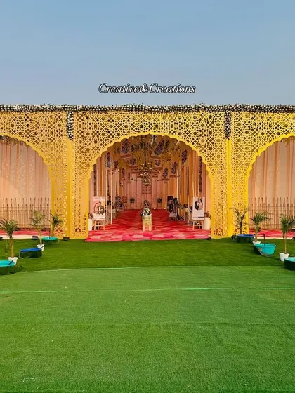 A wide-angle view of a royal wedding entrance. The yellow laser-cut panels create stunning archways, leading guests into the main event area over a lush green carpet.