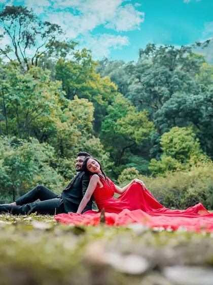 A relaxed and romantic moment from a couple's pre-wedding shoot. This image captures the couple sitting together in a natural setting, showcasing their connection against a lush forest backdrop.