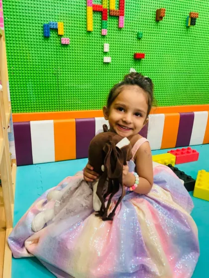A happy girl in our toddler area, which features soft play surfaces and age-appropriate toys like this rocking horse and a Lego wall for creative building.