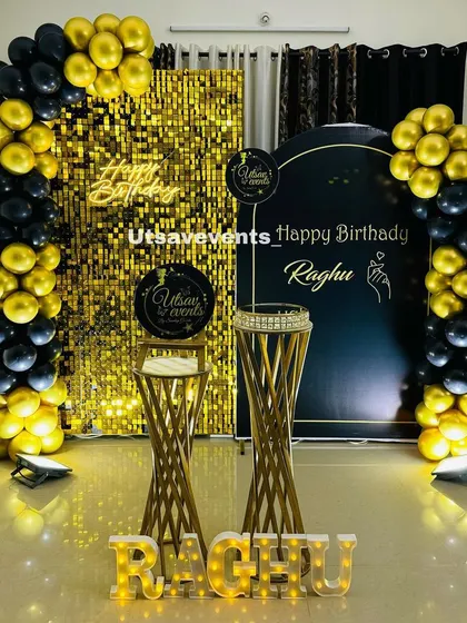 A sophisticated birthday decoration with a gold shimmer wall and a black backdrop panel. The black and gold balloon decor creates a very chic and modern look.