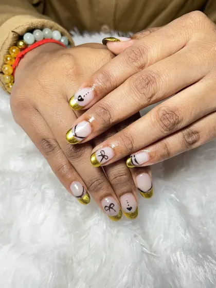 A closer look at the gold chrome French tips with the delicate bow art. The combination of the metallic finish and the cute design is very unique.